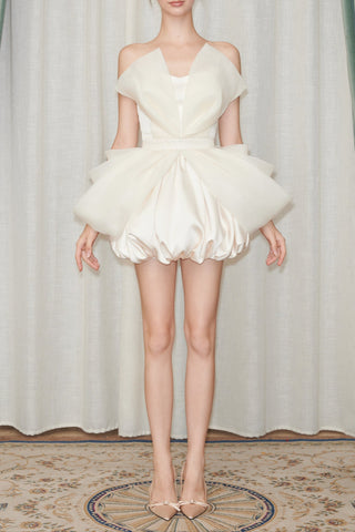 Model wearing a white dress with a ruffled skirt against a curtain backdrop