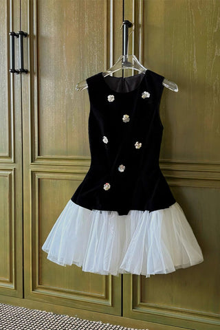 Black dress with white floral embellishments and a white skirt on a hanger against a wooden panel background.