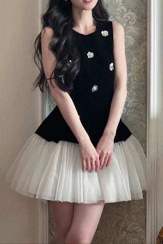 Woman wearing a black top with white floral details and a white pleated skirt against a decorative wall.