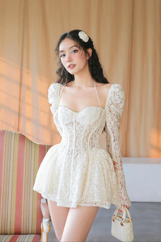 Woman in a white lace dress standing in a softly lit room with curtains.