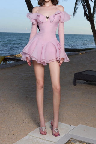 Woman in a pink dress standing on a beach with palm trees and ocean in the background
